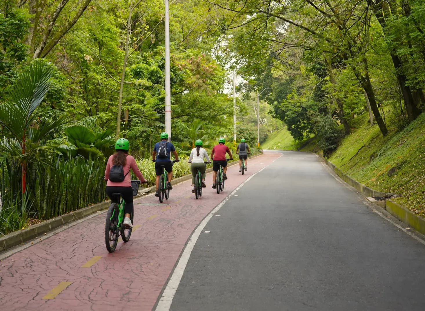 Cyclists on a bike path beside the Medellín River with the Aburrá Valley hills behind