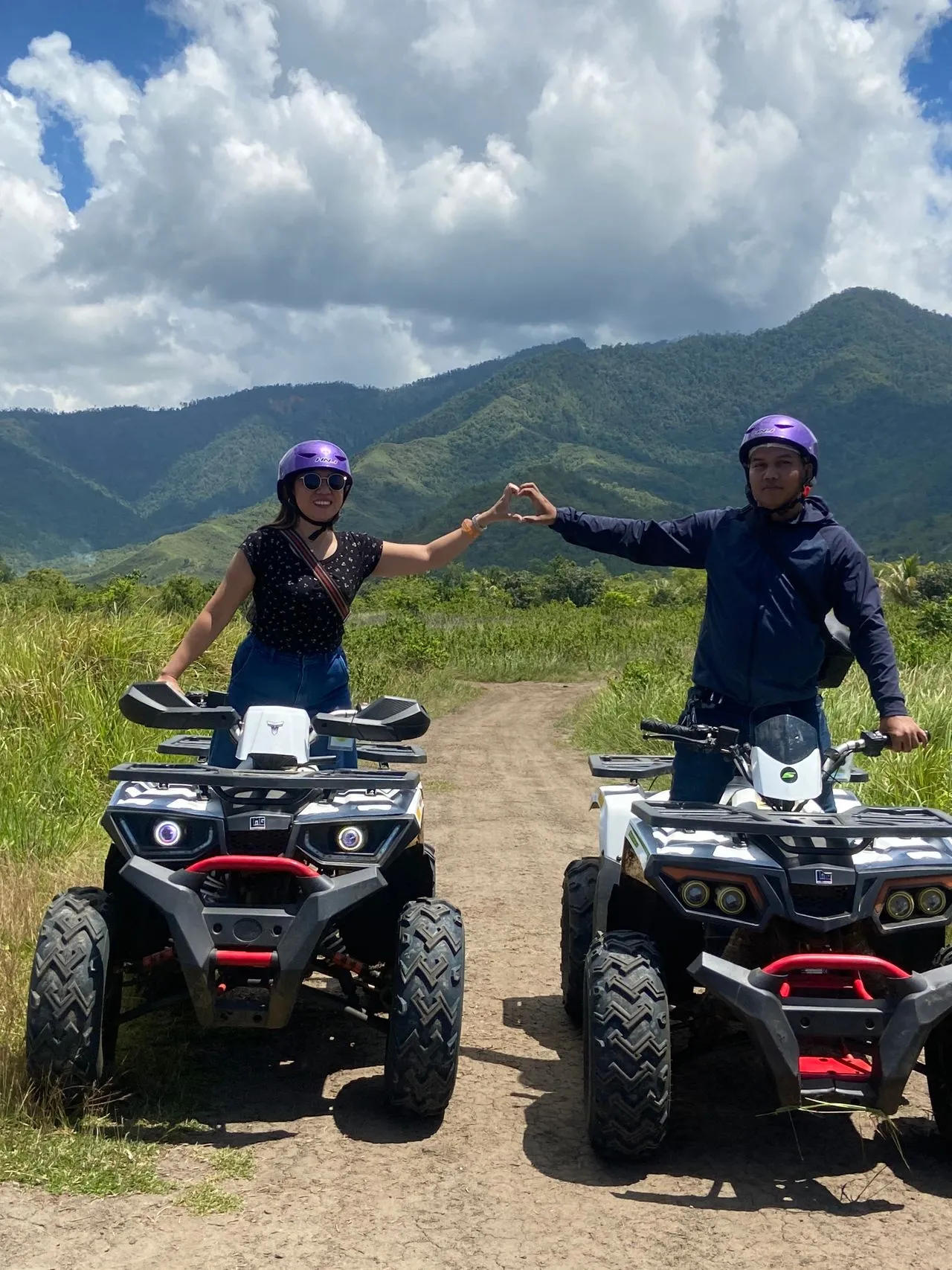 A couple on ATVs forming a heart shape with their arms against a mountainous backdrop in Colombia